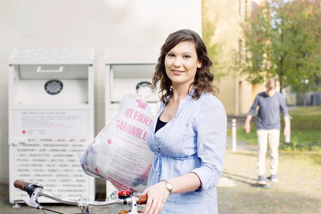 Foto: Eine junge Frau steht mit ihrer Kleiderspende vor zwei DRK-Kleidercontainern.